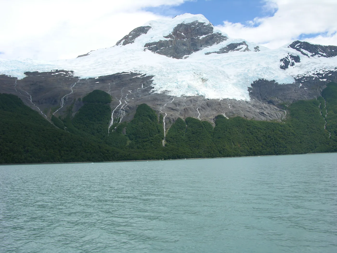 A glacier and snowfields above green forest and a turquoise lake in Los Glaciares, Patagonia